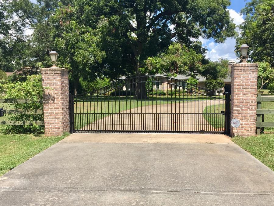 Iron drive gate between brick columns across a concrete driveway