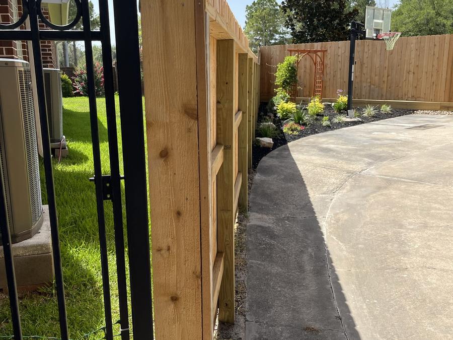 Decorative iron gate panel meeting a cedar fence along a driveway