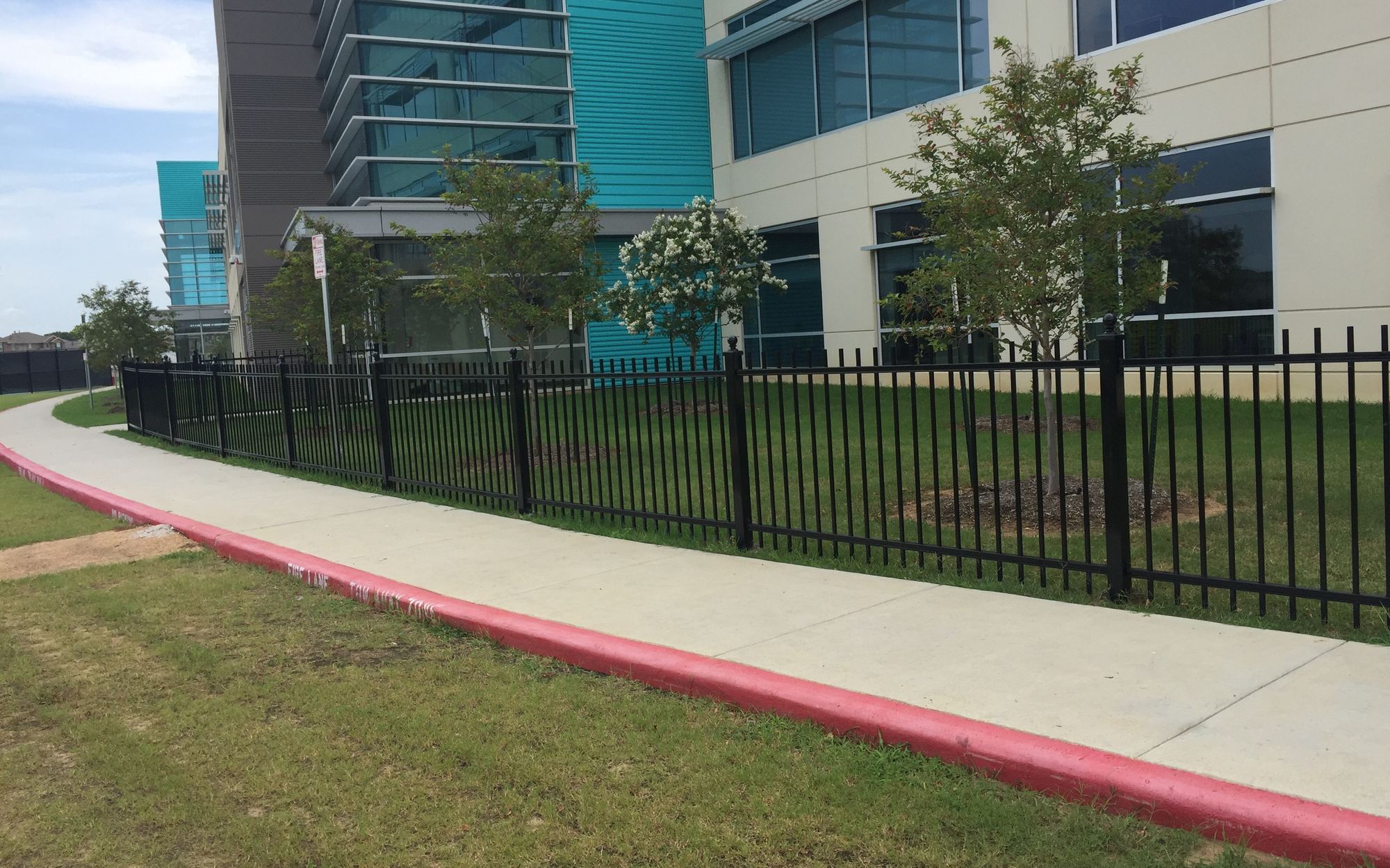 Black ornamental iron fence running alongside a modern Houston corporate campus