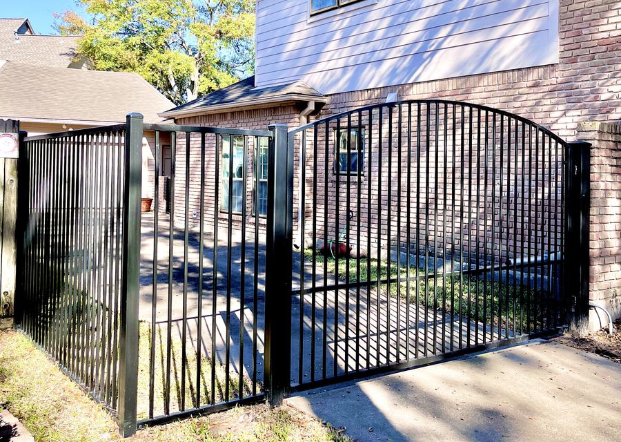Arched black ornamental iron gate between brick columns at a commercial entrance
